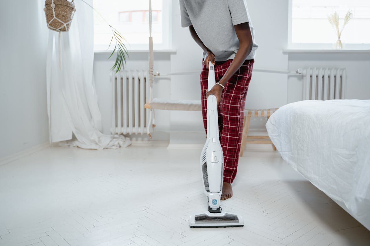 Man cleaning a room with a vacuum cleaner, barefoot in pajamas, ensures tidiness.