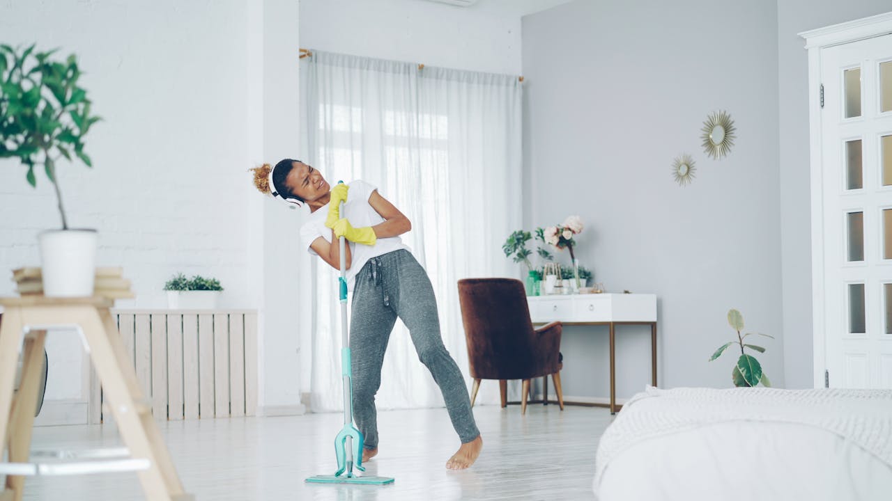 A cheerful woman dances while mopping in a bright, modern living room.